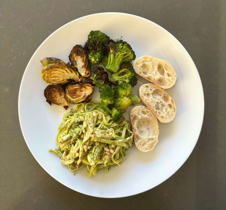 Chicken pesto pasta on a white plate with air-fried Brussels sprouts, broccoli, and bread slices