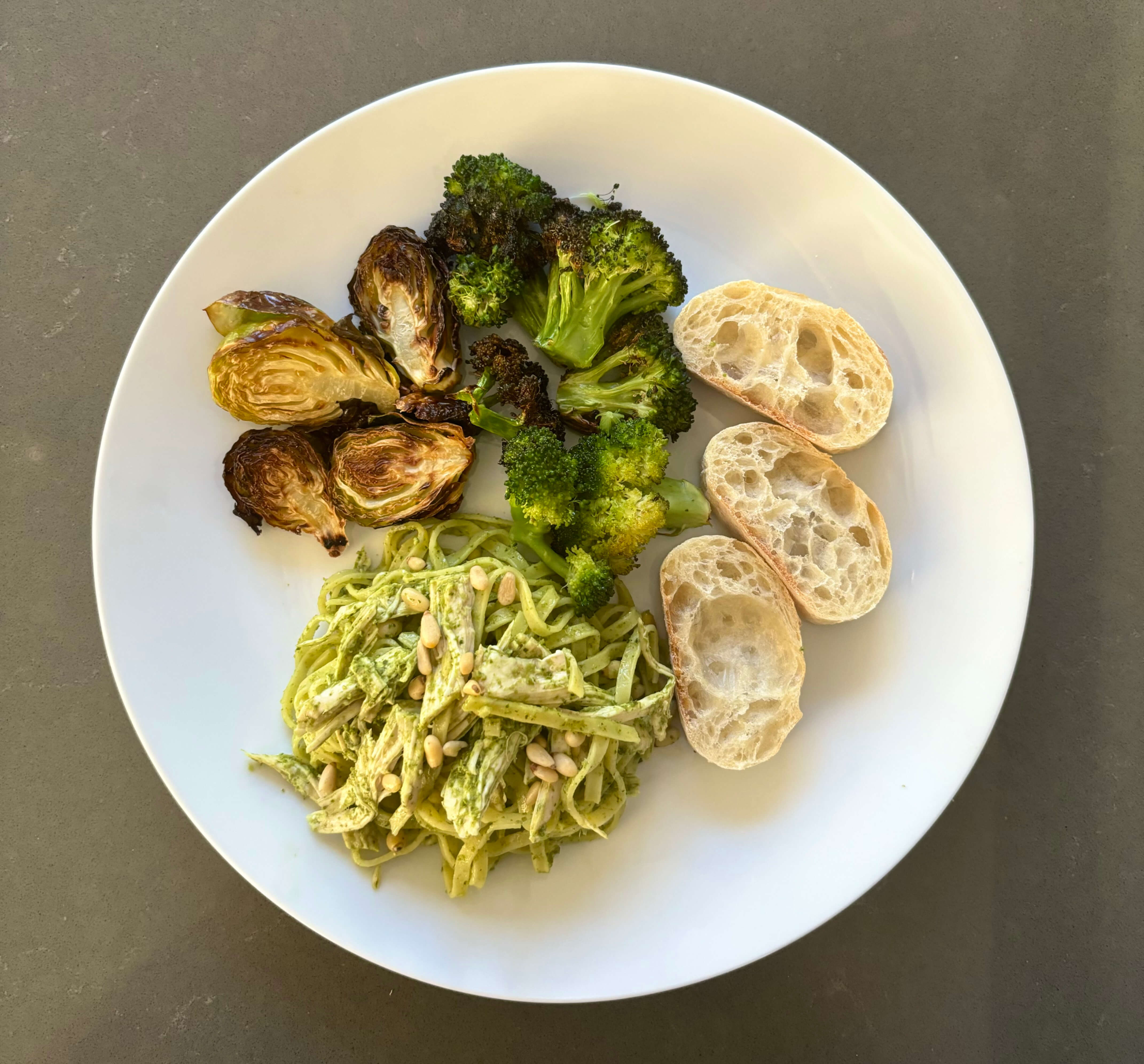 Chicken pesto pasta on a white plate with air-fried Brussels sprouts, broccoli, and bread slices